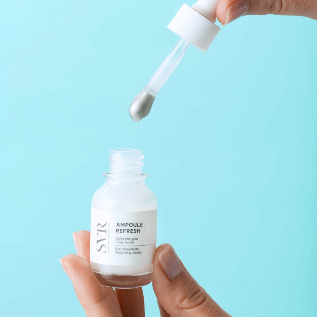 SVR Ampoule Refresh Augenserum in kleiner Glasflasche mit metallischer Massage-Pipette vor hellblauem Hintergrund.