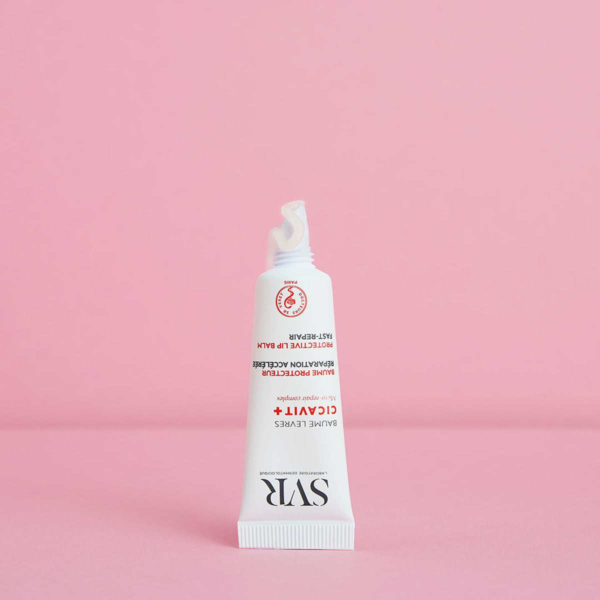 SVR Cicavit+ Lippenbalsam in einer weißen Tube mit roter Schrift und austretender transparenter Textur auf rosa Hintergrund.