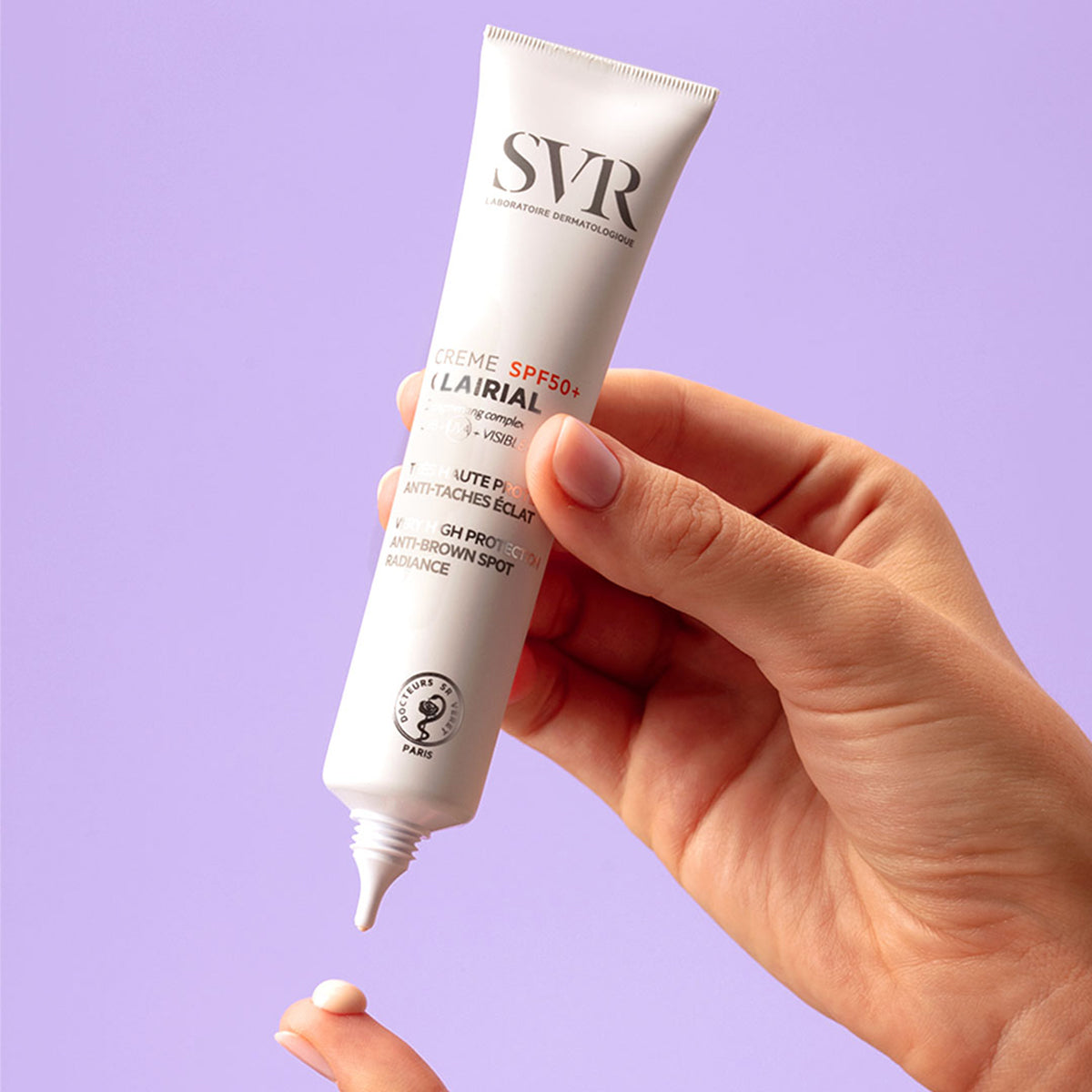 Hand hält eine weiße SVR Clairial Crème SPF50+ Tube, aus der ein kleiner Klecks Creme auf den Finger gedrückt wird.