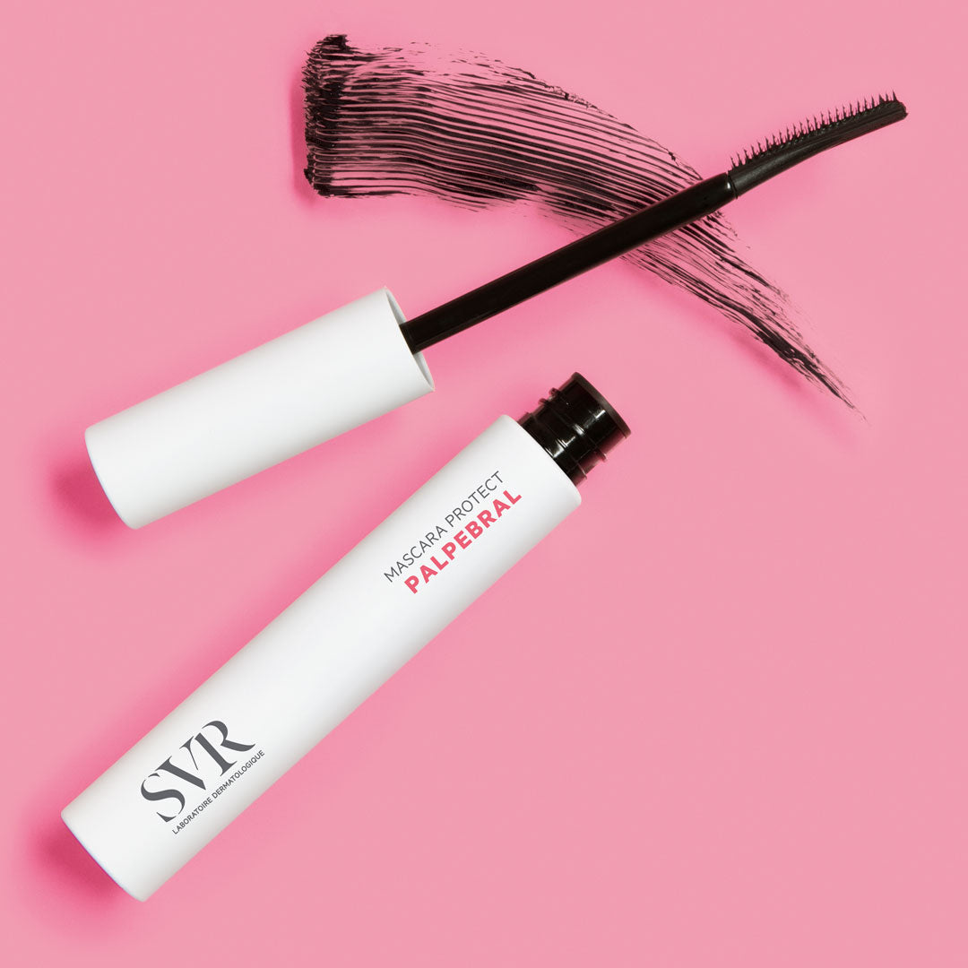 SVR PALPEBRAL Mascara Protect in weißer Tube mit schwarzem Bürstenapplikator und schwarzem Wimperntusche-Abstrich auf rosa Hintergrund.