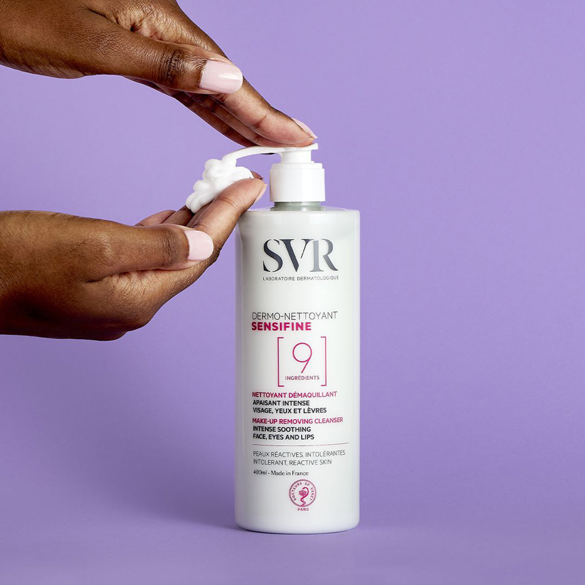 Weiße SVR Sensifine Dermo-Nettoyant Reinigungsflasche mit Pumpspender und weißer Gelcreme auf lila Hintergrund.