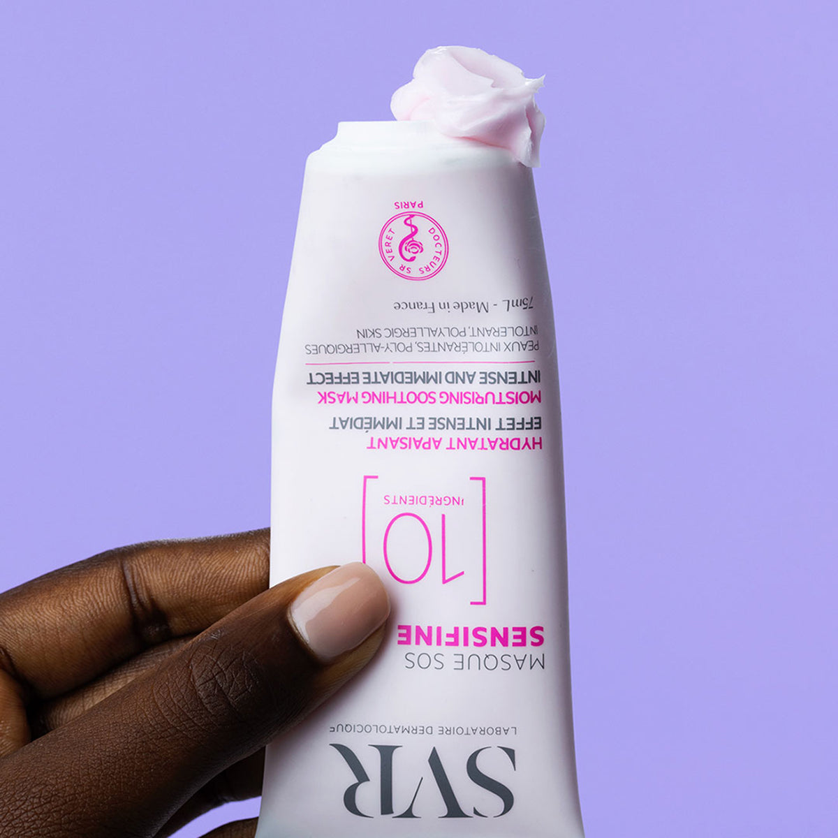 Weiße 75ml SVR Sensifine SOS Maske Tube mit rosa Creme-Textur in einer Hand vor lila Hintergrund.