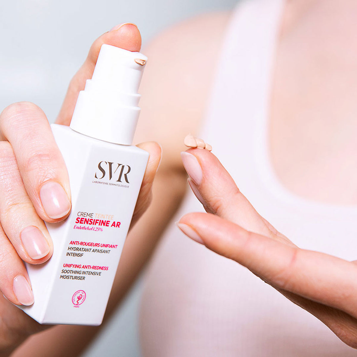Weiße SVR Sensifine AR Crème Teintée Pumpspenderflasche mit getönter Creme auf dem Finger zur Rötungskorrektur.
