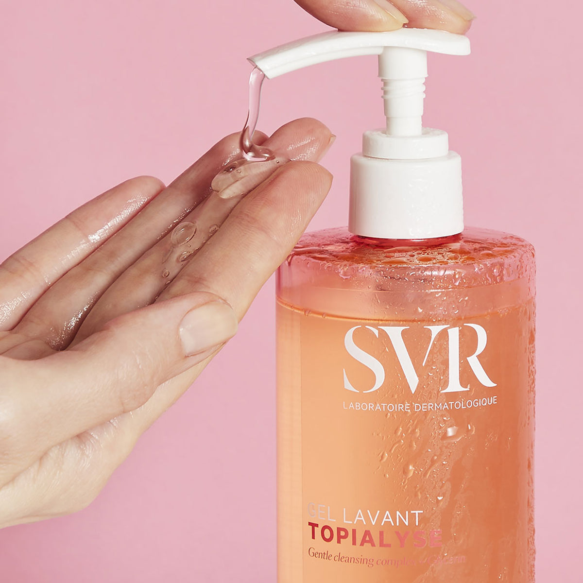 Transparente SVR TOPIALYSE Gel lavant Flasche mit weißem Pumpspender, aus der klares Reinigungsgel auf eine Hand fließt.