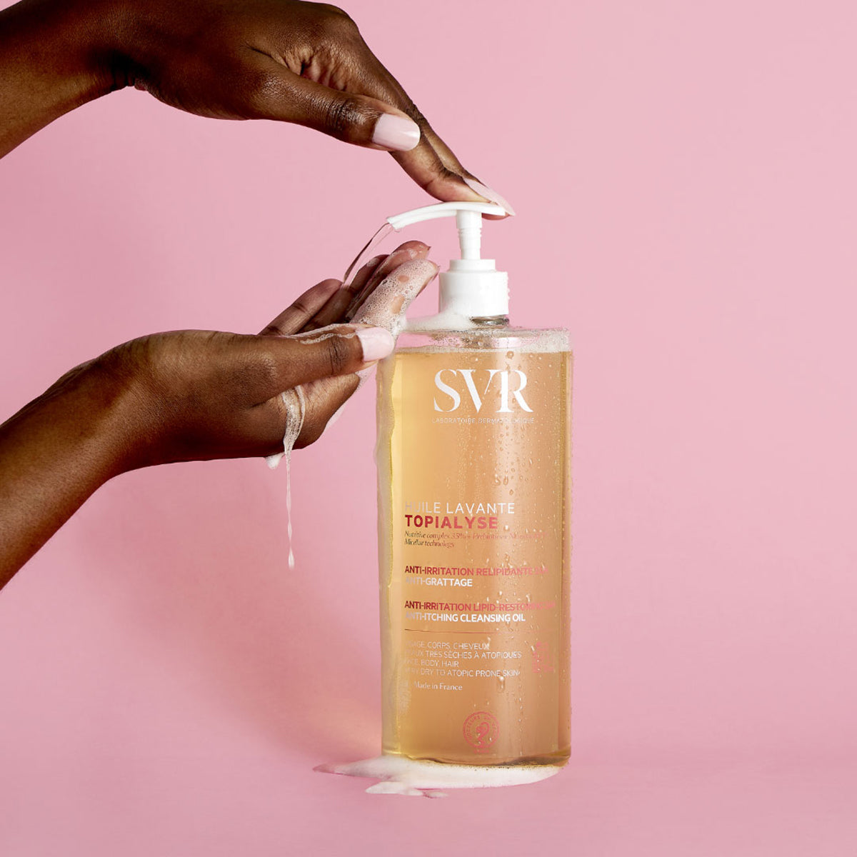 SVR Topialyse Huile Lavante Reinigungsöl in einer transparenten Pumpflasche mit Schaum auf rosa Hintergrund.