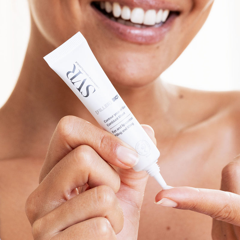 Weiße SVR Biotic Filler Tube für Augen- und Lippenpflege, aufgetragen auf den Finger einer lächelnden Frau.