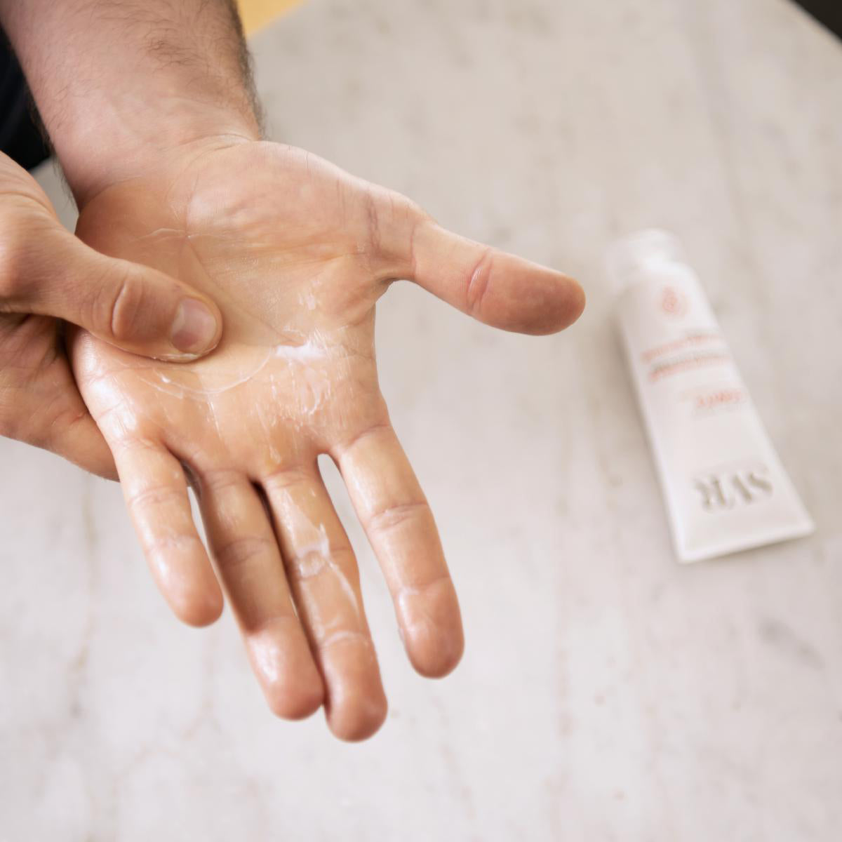 Weiße Cicavit+ Handcreme auf der Handfläche einer Person, daneben eine SVR-Tube auf einem hellen Marmortisch.