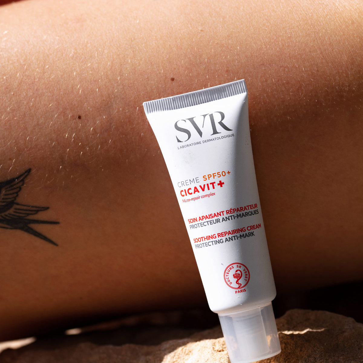 Weiße SVR Cicavit+ SPF50+ Creme-Tube vor sonnengebräunter Haut mit Tattoo im Freien bei Sonnenlicht.