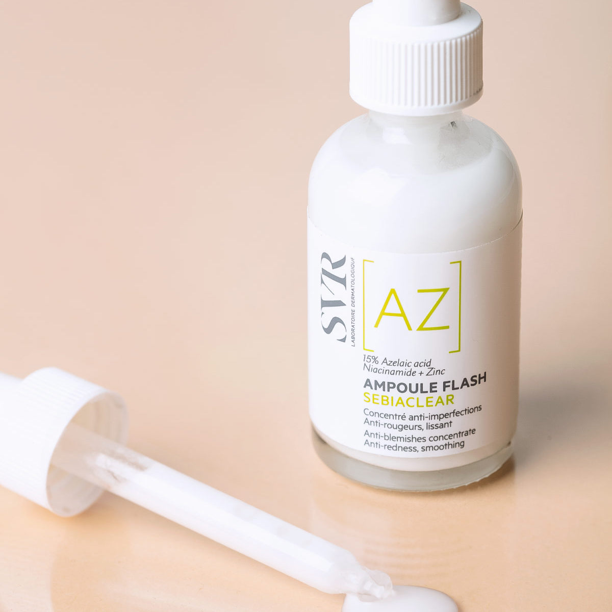 SVR Sebiaclear Ampoule Flash mit weißem Serum, Pipette und Etikett mit Azelainsäure auf beigem Hintergrund.