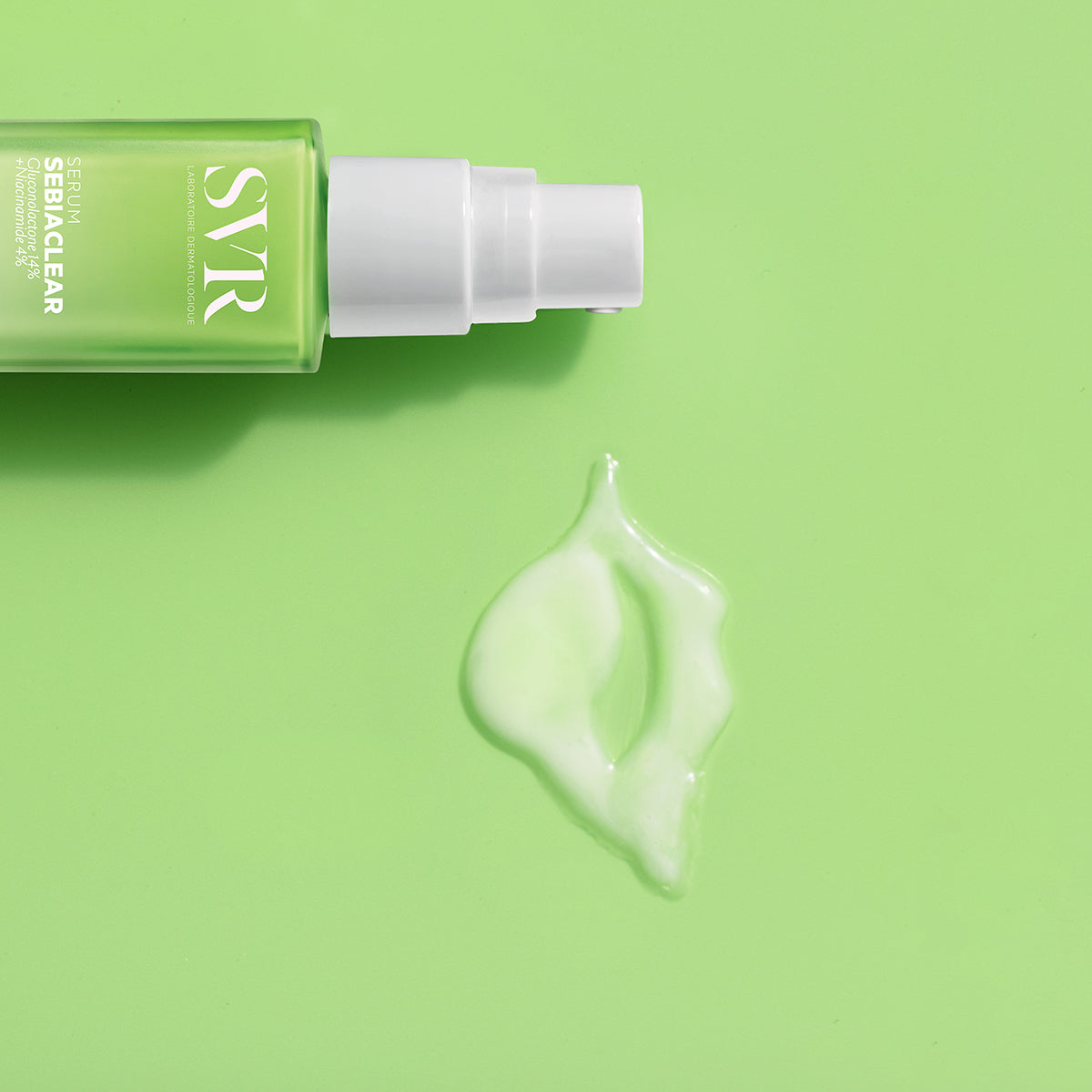SVR SEBIACLEAR Serum in einer grünen Glasflasche mit weißem Pumpspender und einem Tropfen der Textur auf hellgrünem Hintergrund.