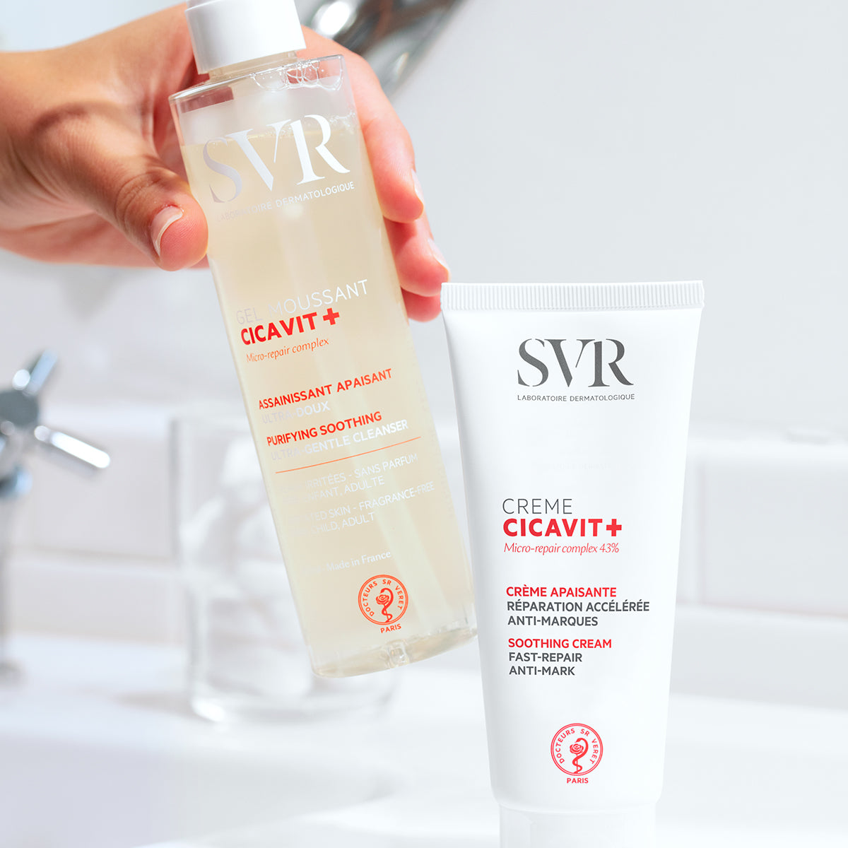 SVR Cicavit+ Reinigungs-Gel und Repair-Creme in weißer Tube und transparenter Flasche vor einem Badezimmer-Waschbecken.