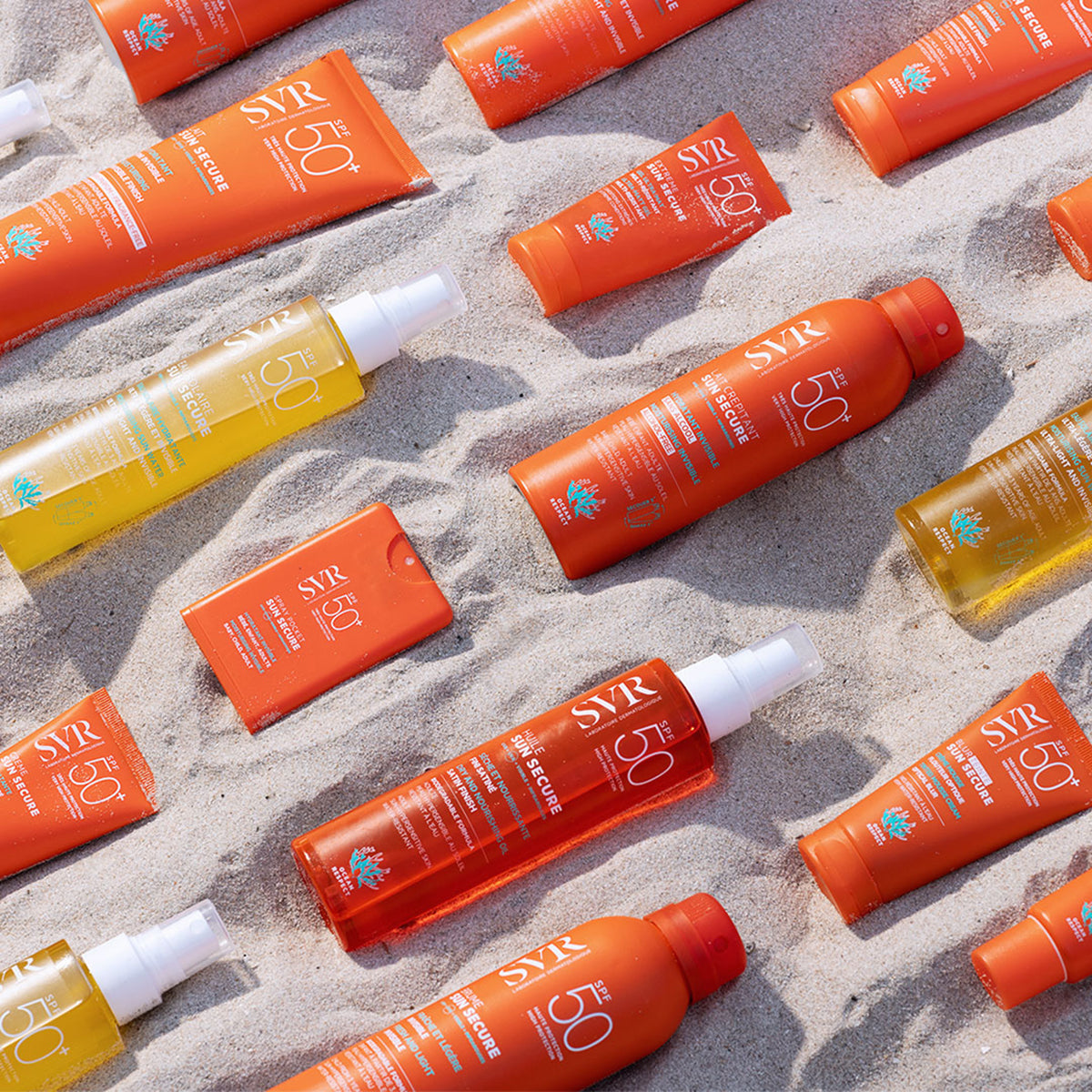 Verschiedene SVR Sun Secure SPF50+ Sonnenschutzprodukte in orangefarbenen Tuben und Flaschen auf hellem Sand am Strand.