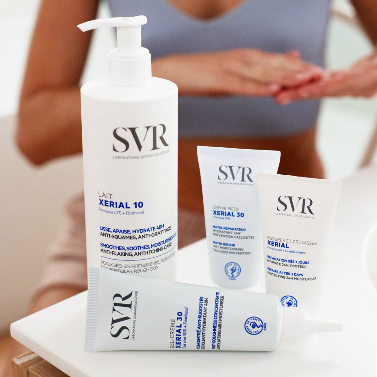 SVR XERIAL Hautpflegeprodukte: eine große Pumpflasche und drei weiße Tuben mit blauer Beschriftung auf einem weißen Tisch.