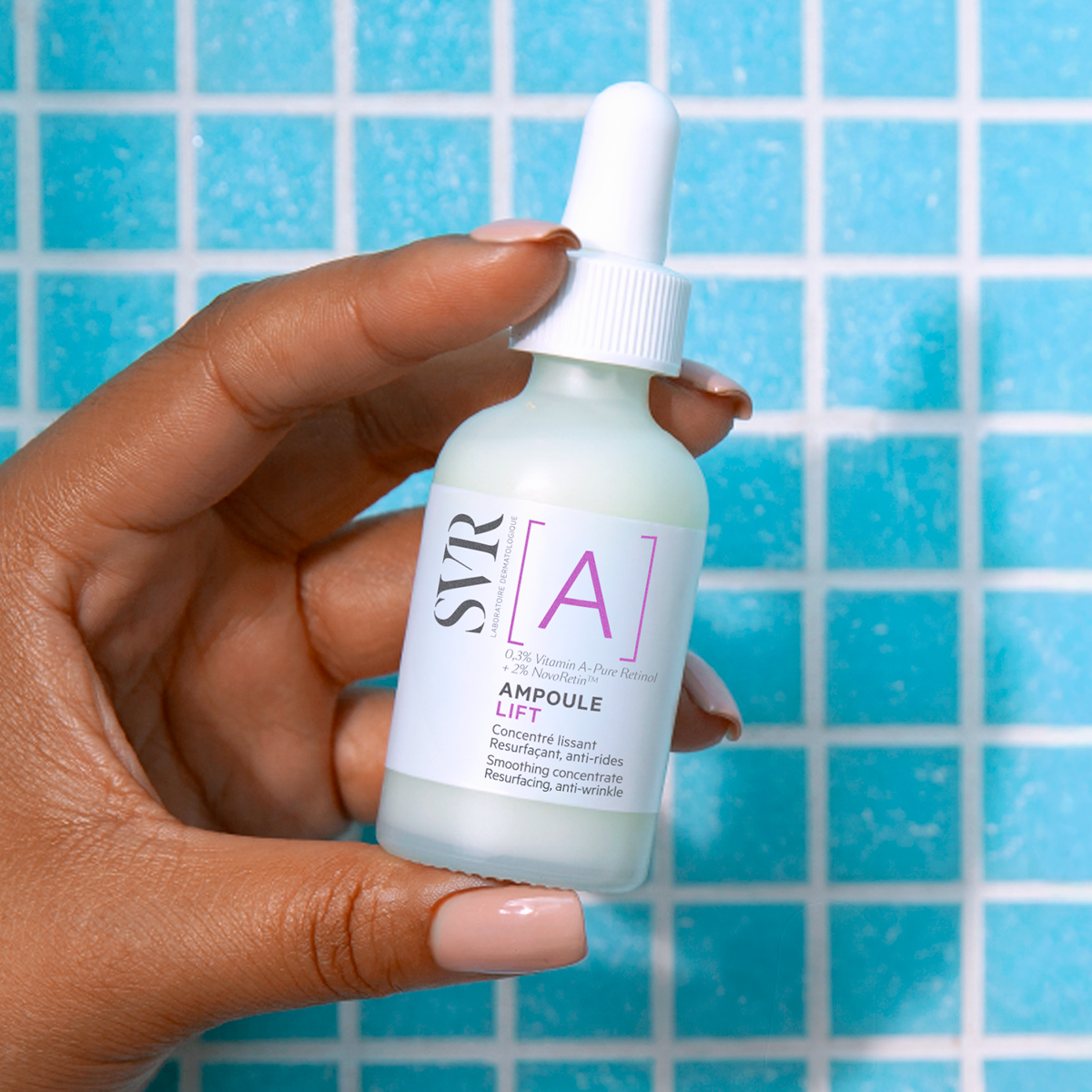 Hand holding a white glass bottle of SVR Ampoule Lift serum with a dropper cap against a blue tiled background.