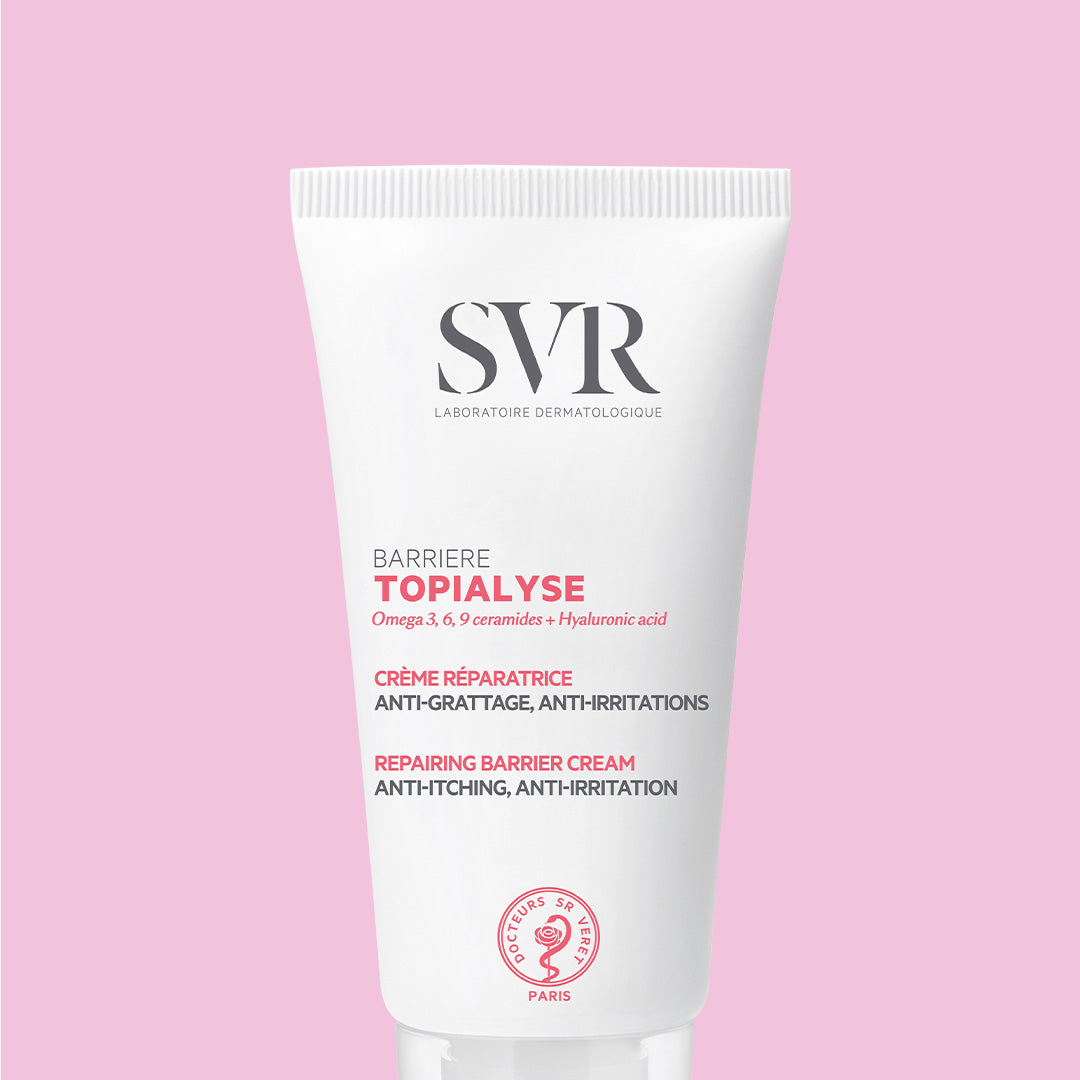 Weiße SVR TOPIALYSE Barrière Reparaturcreme in einer Tube vor einem zartrosa Hintergrund.