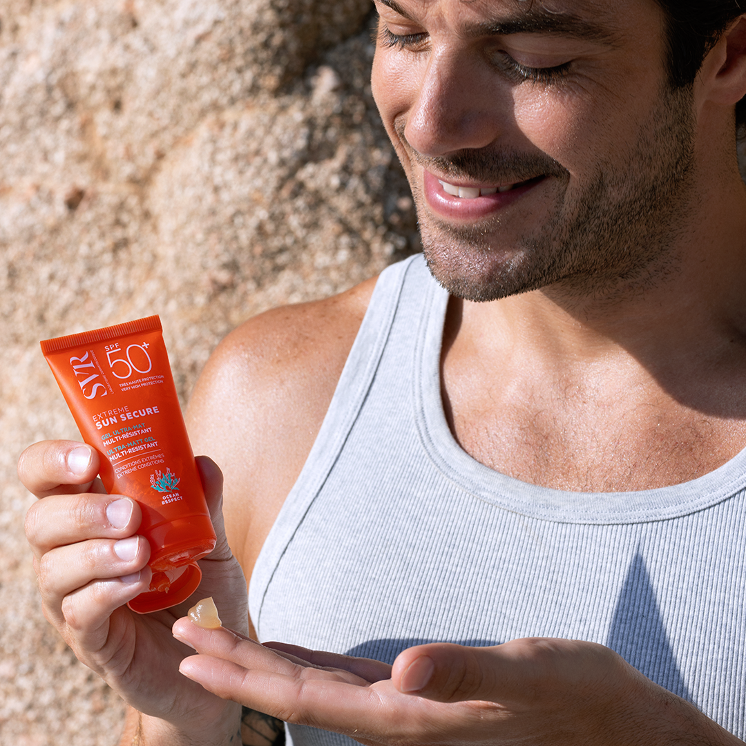 Man applying SVR Sun Secure SPF 50+ ultra-matt gel from an orange tube onto his palm outdoors.