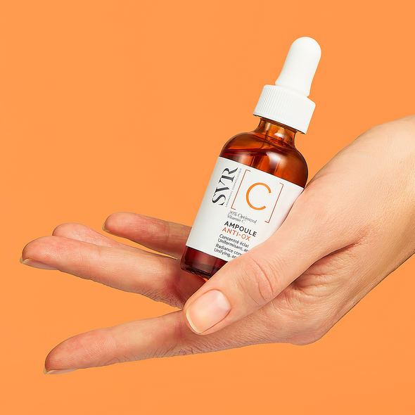 Hand hält SVR Ampoule Anti-Ox Serum in einer braunen Glasflasche mit weißer Pipette vor orangefarbenem Hintergrund.