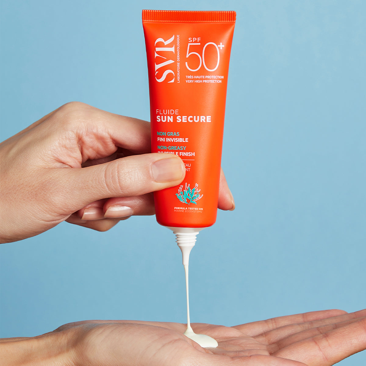 Orangefarbene SVR SUN SECURE Fluide SPF50+ Tube, aus der weiße Sonnencreme auf eine Handfläche fließt, vor blauem Hintergrund.