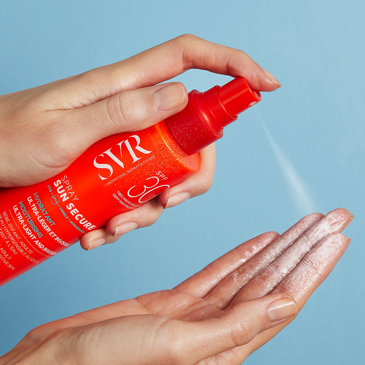 Hand sprüht SVR SUN SECURE SPF30 Sonnenschutzspray mit milchiger Textur auf die Handfläche vor hellblauem Hintergrund.