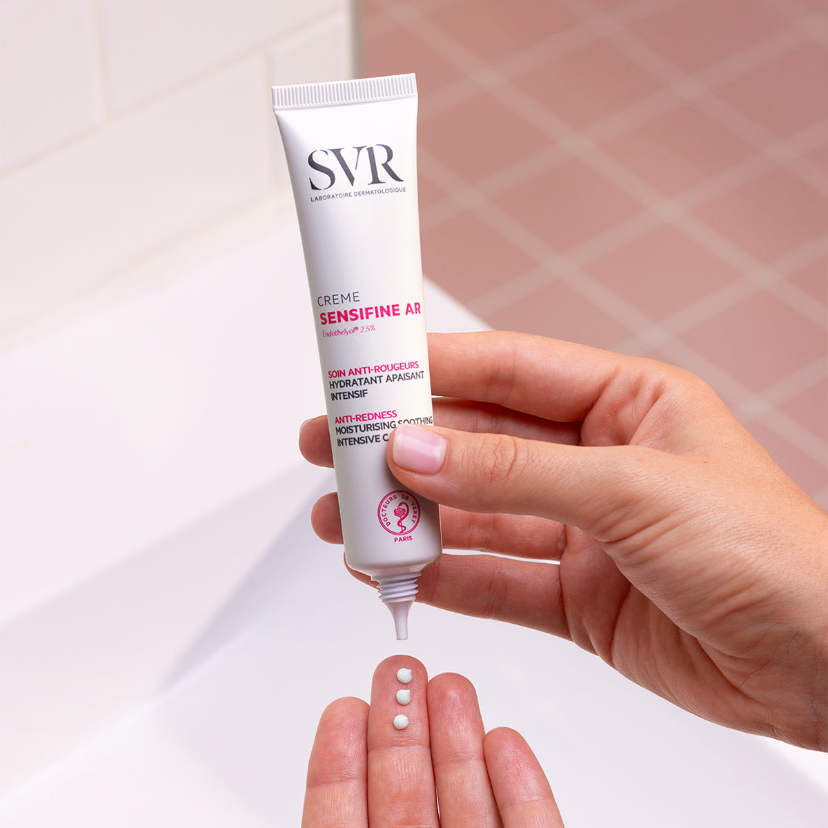 Weiße SVR Sensifine AR Creme Tube in der Hand, die drei kleine Cremepunkte auf die Handfläche abgibt.