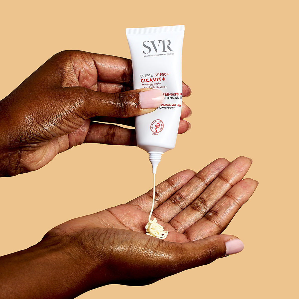 Weiße SVR CICAVIT+ SPF50+ Tube, aus der eine cremige Textur auf eine Handfläche gedrückt wird, vor beigem Hintergrund.