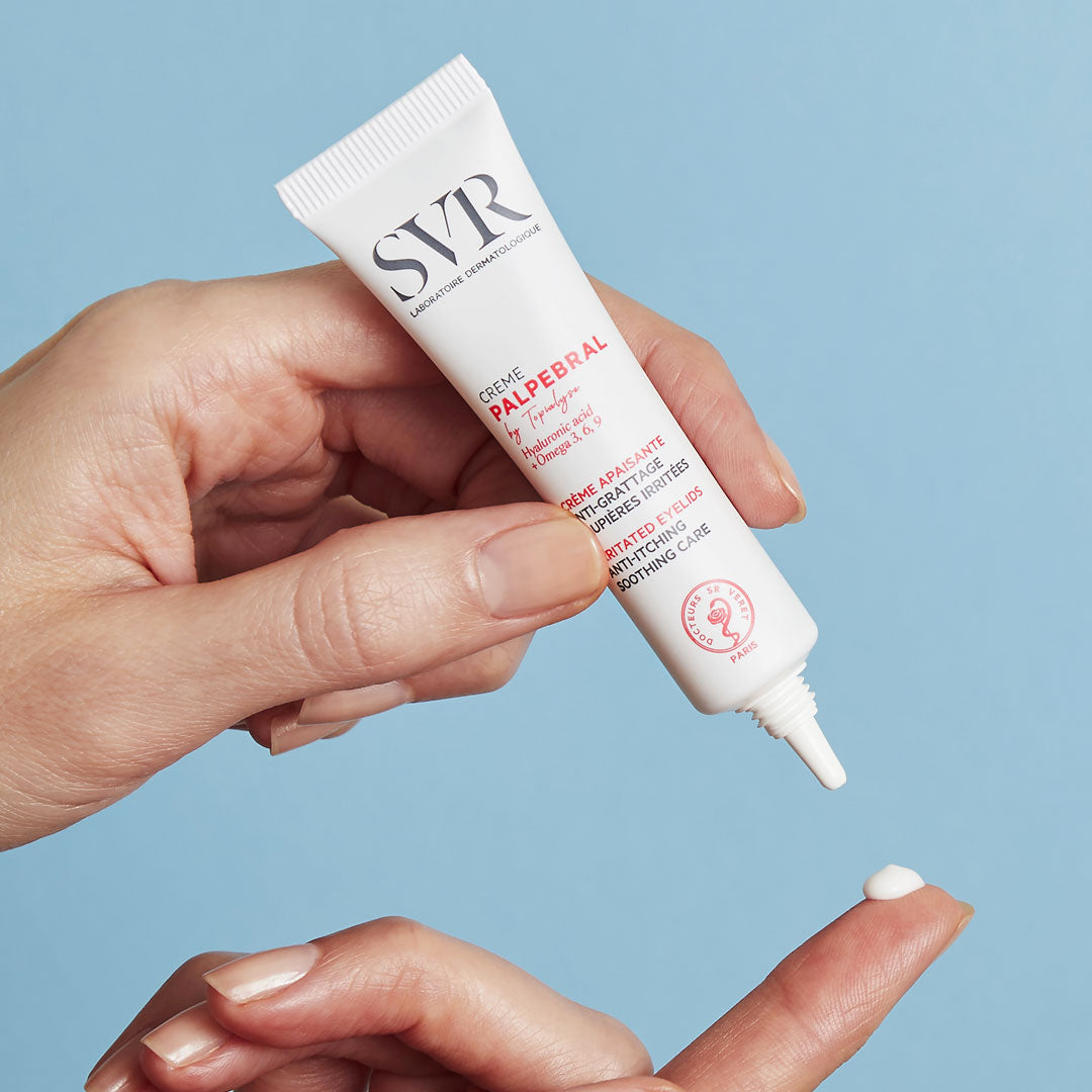 Weiße SVR Palpebral Augencreme-Tube in der Hand, die eine kleine Menge der weißen Textur auf den Finger abgibt.