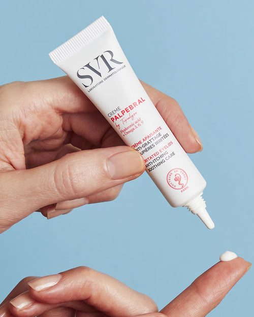 Weiße SVR Palpebral Augencreme-Tube in der Hand, die eine kleine Menge der weißen Textur auf den Finger abgibt.