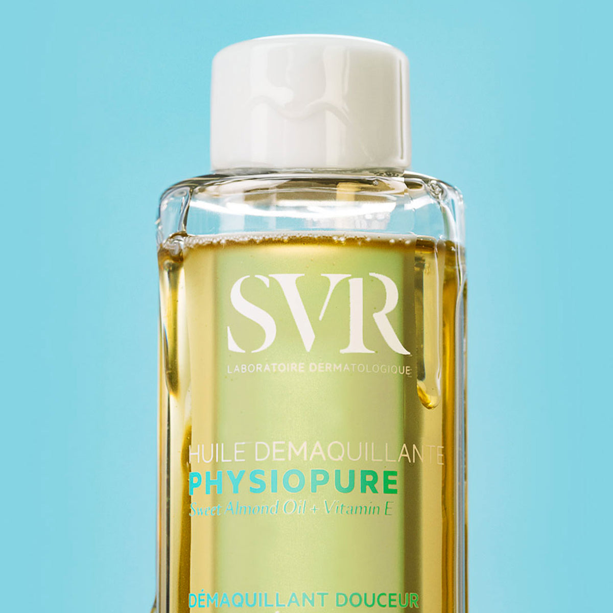 Transparente Flasche mit SVR PHYSIOPURE Reinigungsöl, goldener Textur und weißem Verschluss vor hellblauem Hintergrund.