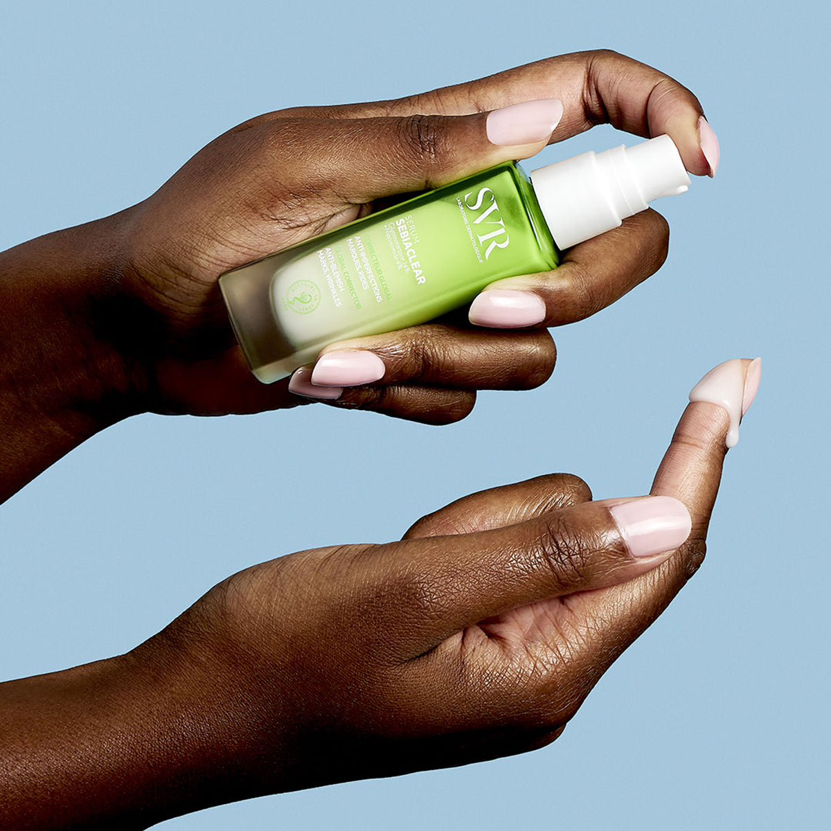 SVR Sebiaclear Serum in einer grünen Glasflasche mit weißem Pumpspender, aufgetragen auf einen Finger vor blauem Hintergrund.