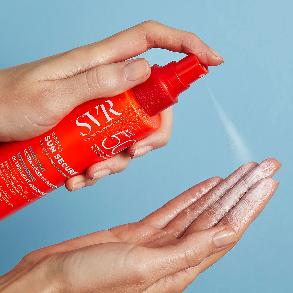 Hand sprüht SVR SUN SECURE SPF50+ Sonnenschutzspray aus der leuchtend orangen Flasche auf die Handfläche.