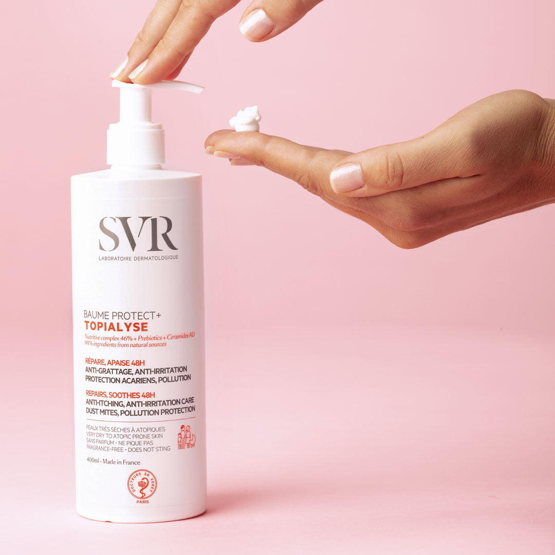 Weiße SVR Topialyse Baume Protect+ Pumpflasche mit weißer Creme auf einer Hand vor einem hellrosa Hintergrund.