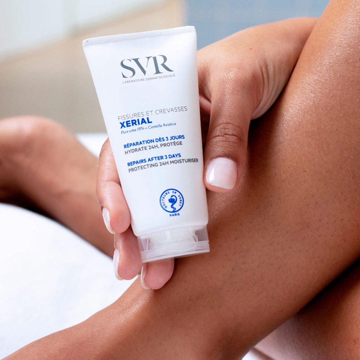 Weiße SVR XERIAL Fissures & Crevasses Creme-Tube in einer Hand, die auf einem Bein ruht, für rissige und trockene Füße.