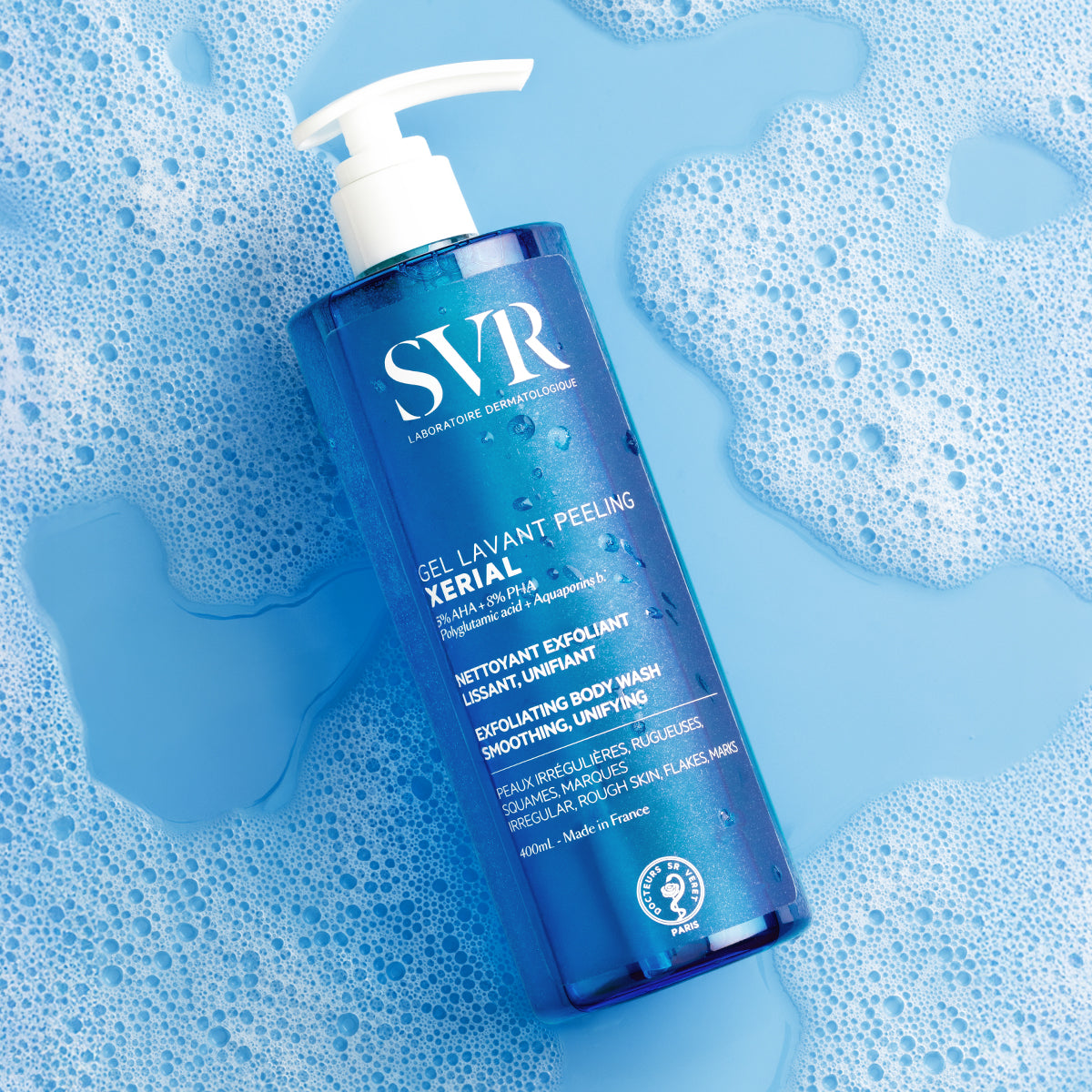 SVR XERIAL Gel Lavant Peeling 400ml bottle with white pump, surrounded by blue soap bubbles and water on a light blue background.
