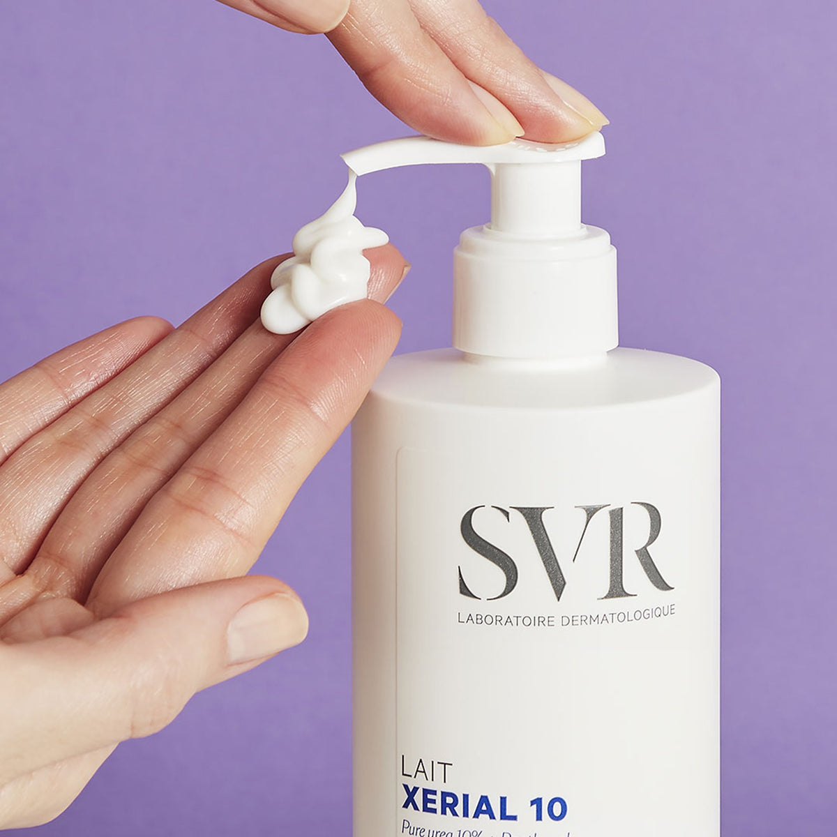 Weiße SVR XERIAL 10 Lait Pumpflasche mit cremiger Textur auf der Hand vor lila Hintergrund.