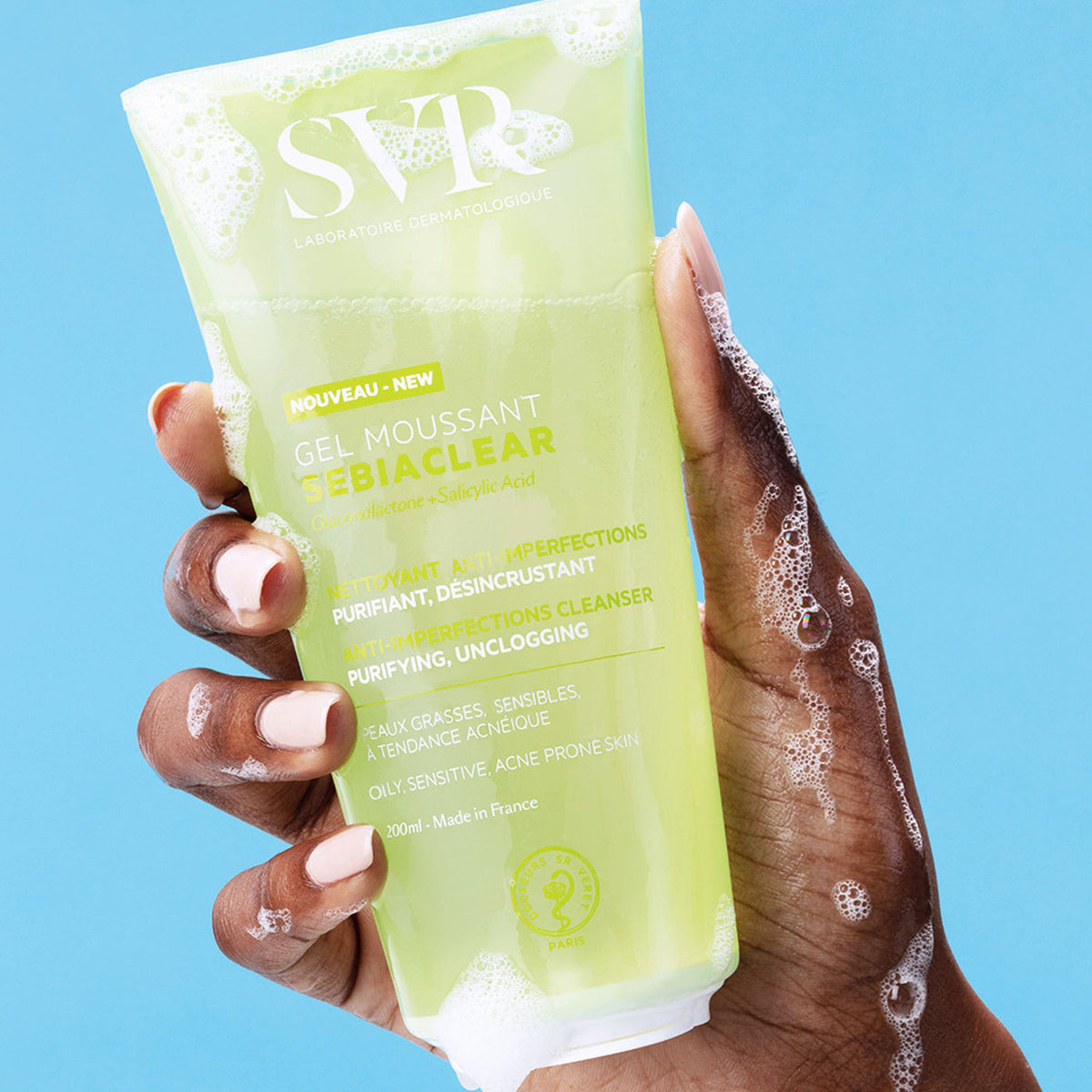 SVR SEBIACLEAR Gel Moussant 200ml Tube in einer Hand mit Schaum vor hellblauem Hintergrund.