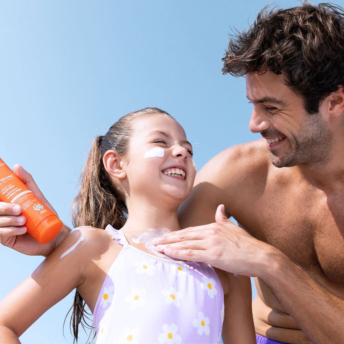 Vater trägt SUN SECURE Lait SPF50+ Sonnenmilch auf die Schultern seiner lachenden Tochter auf.