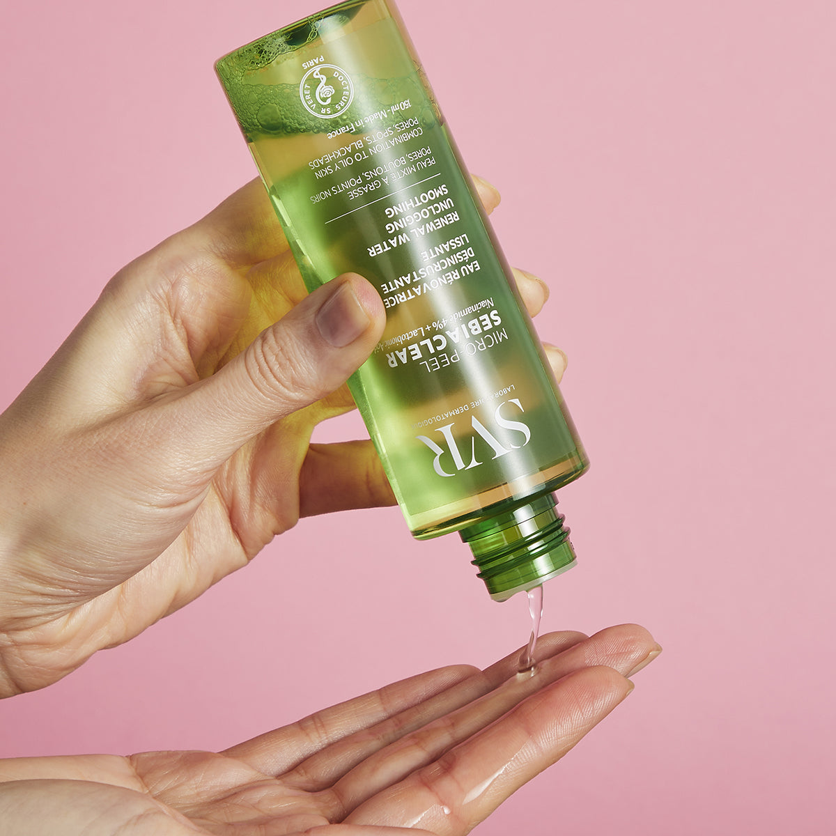 Transparente grüne SVR SEBIACLEAR Micro-Peel Flasche, aus der flüssige Lotion auf eine Handfläche geträufelt wird.