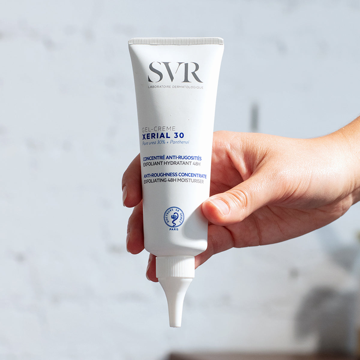 Weiße SVR XERIAL 30 Gel-Crème Tube mit Präzisionsspitze, gehalten in einer Hand vor hellem Hintergrund.