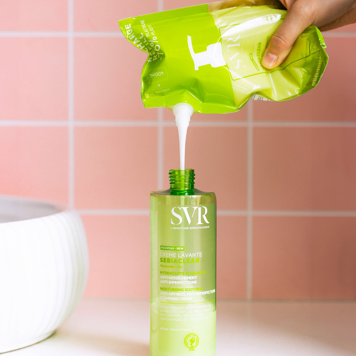 SVR SEBIACLEAR Waschcreme Nachfüllbeutel wird in eine grüne 400ml Kunststoffflasche vor rosa Fliesen gefüllt.