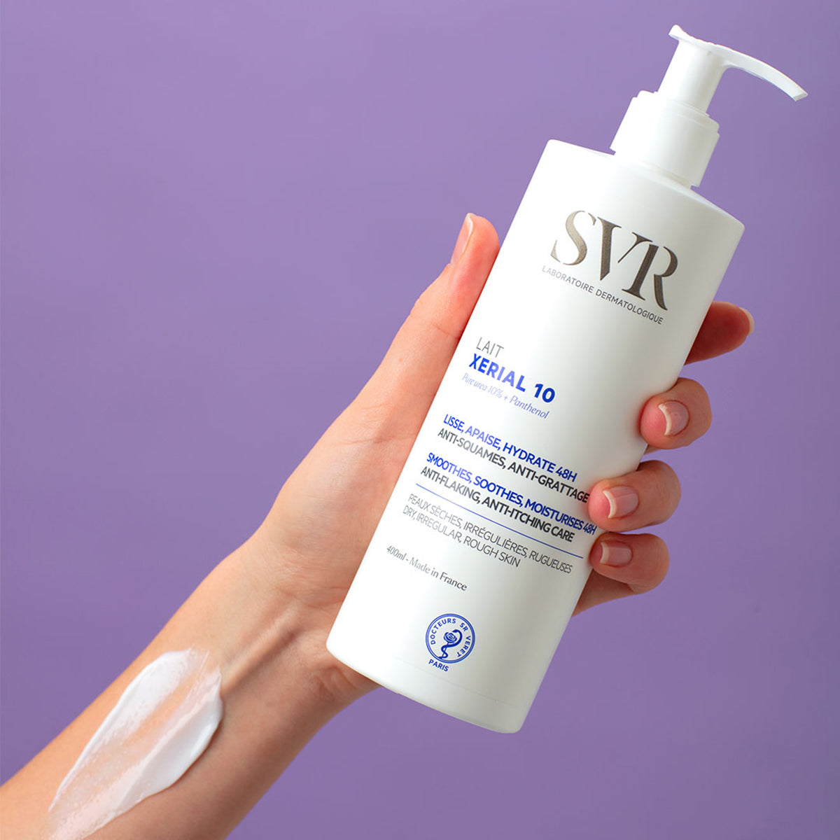 Weiße SVR XERIAL 10 Lait Pumpflasche (400ml) in der Hand gehalten mit einer Texturprobe der Körperlotion auf dem Unterarm.