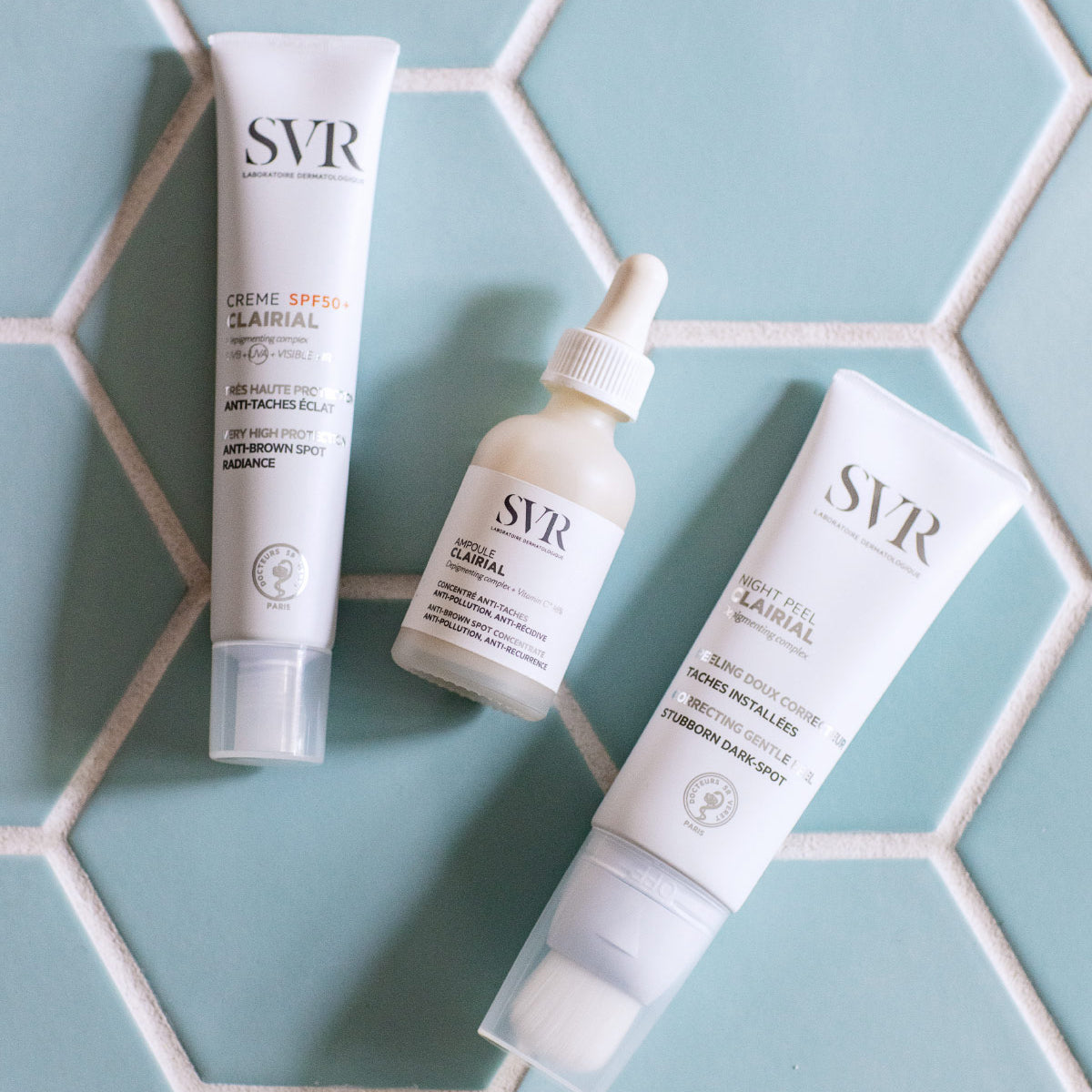 SVR Clairial Hautpflege-Set bestehend aus Creme SPF50+, Ampulle und Night Peel auf hellblauen Fliesen.