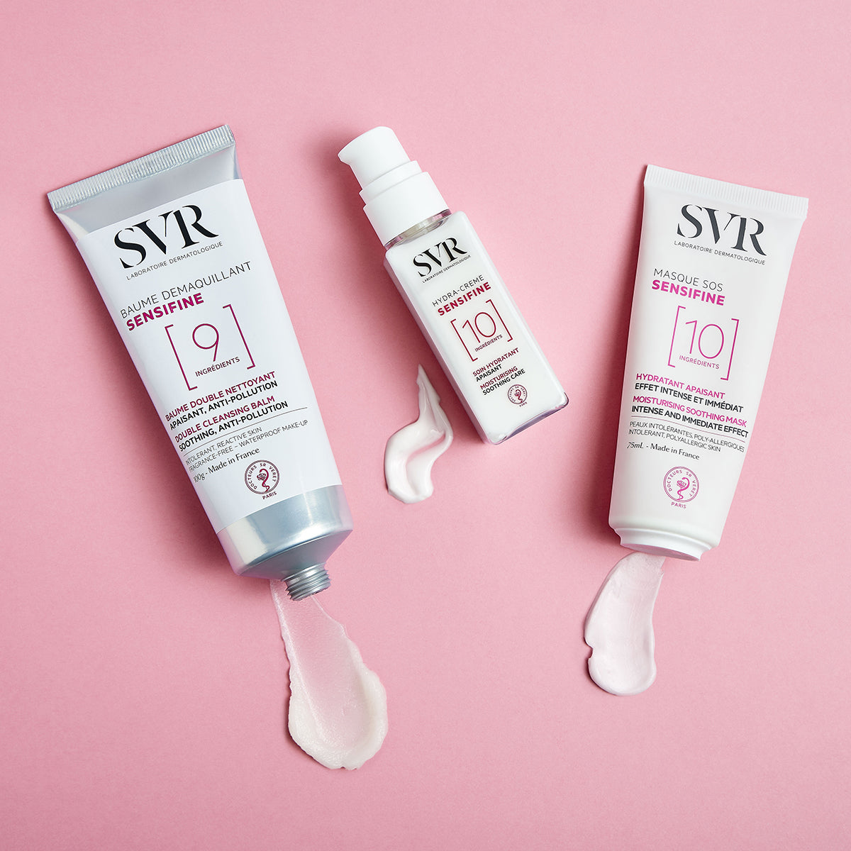 SVR Sensifine Hautpflege-Produkte in weißen Tuben und Flaschen mit cremigen Texturen auf einem rosa Hintergrund.