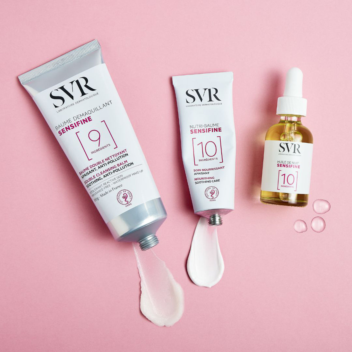 SVR Sensifine Pflegeprodukte in Aluminiumtuben und Glasflasche mit cremiger Textur auf rosa Hintergrund.