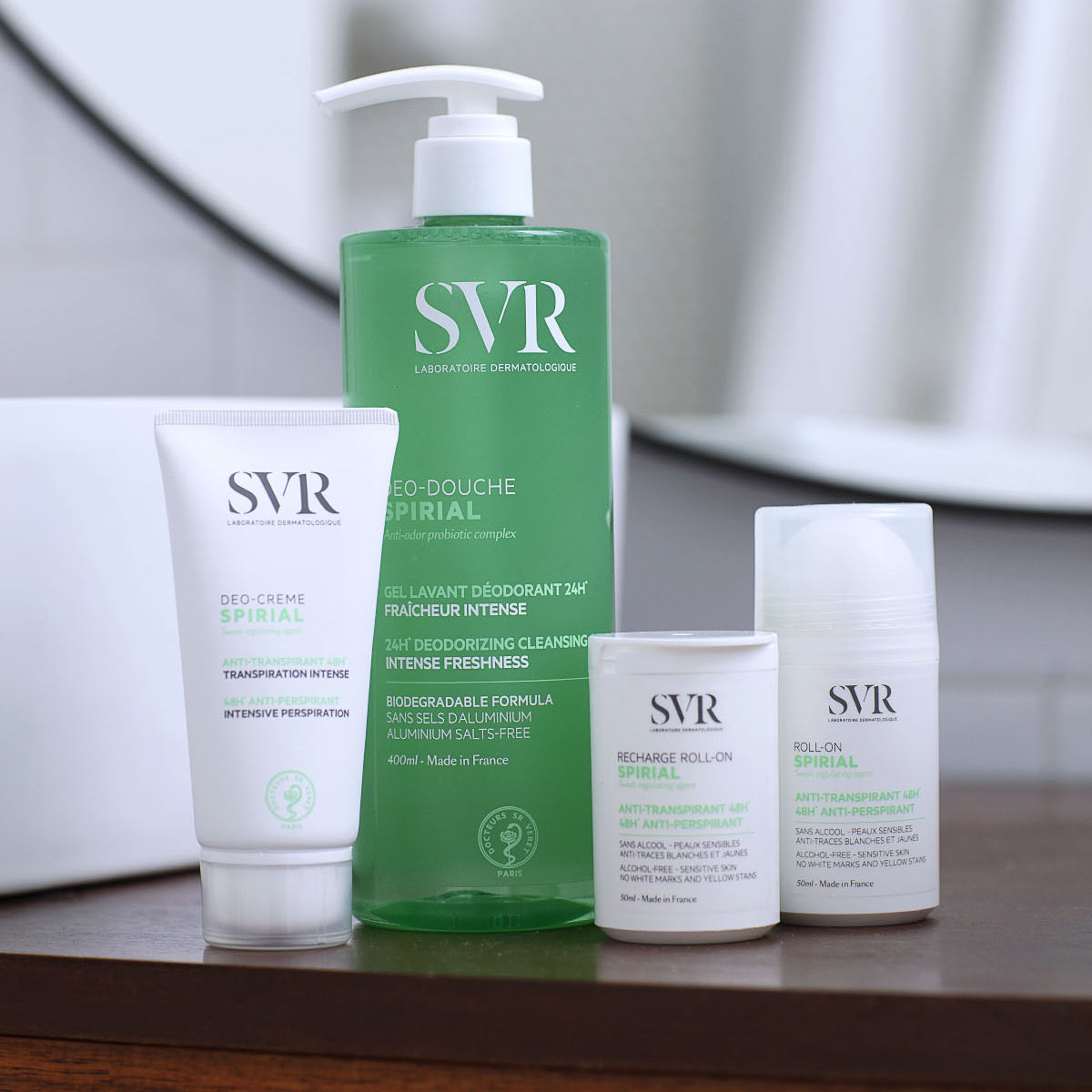 SVR Spirial Produktreihe mit grünem Duschgel, weißer Deo-Creme und zwei Roll-on Deodorants auf einem Holzregal.