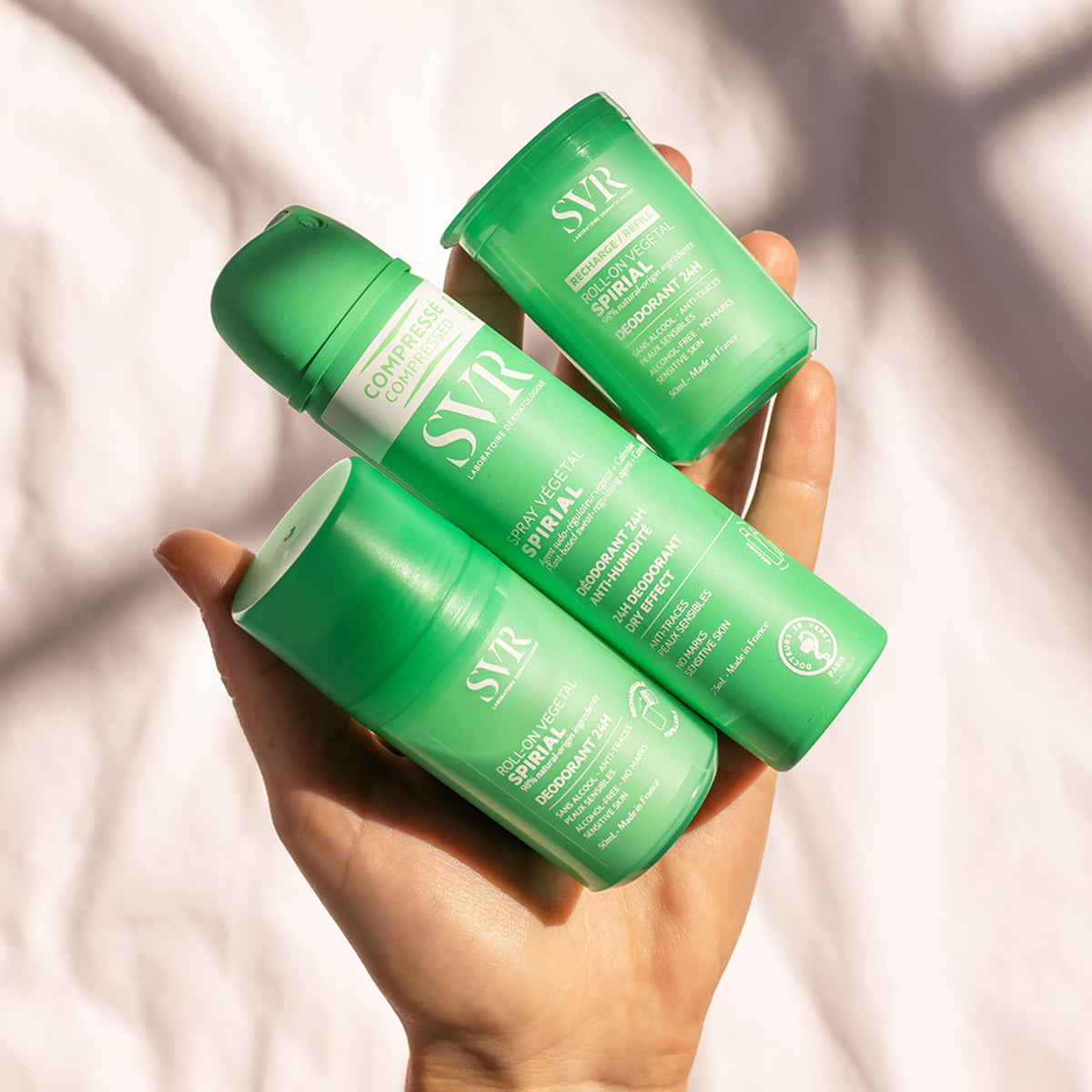 Hand hält drei grüne SVR Spirial Deodorant-Produkte in Spray- und Roll-on-Formaten vor hellem Hintergrund.
