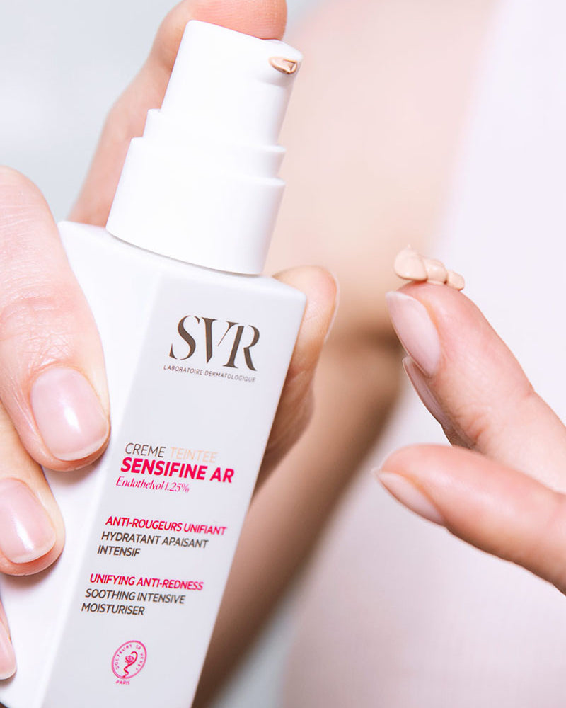 SVR Sensifine AR tinted cream bottle with a pump, showing a drop of beige moisturizer on a finger.