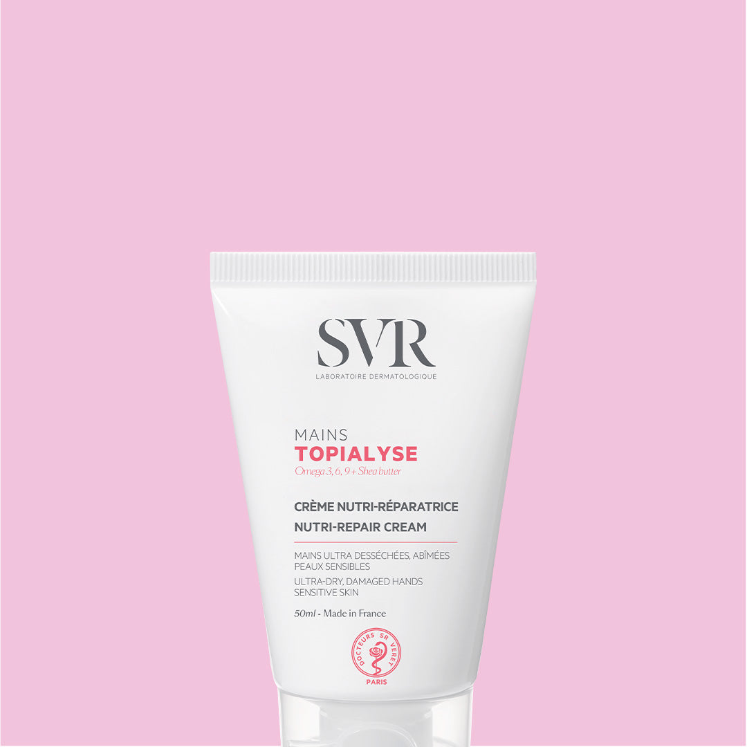 Weiße 50ml SVR TOPIALYSE Handcreme-Tube mit schwarzer und roter Beschriftung vor einem hellrosa Hintergrund.