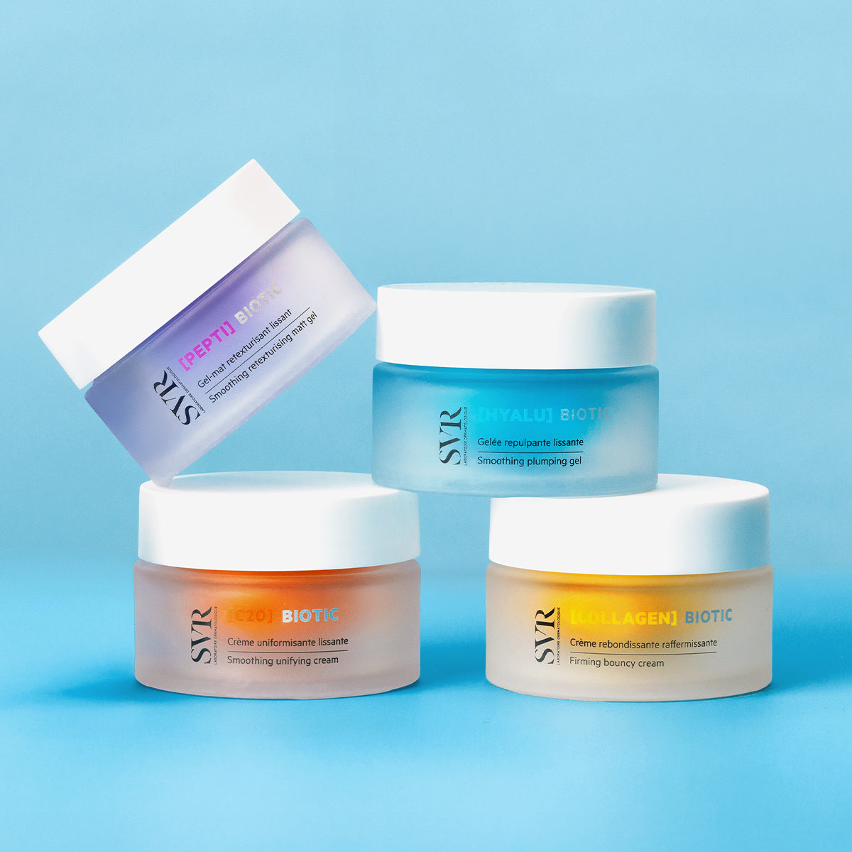 Four SVR Biotic skincare jars in purple, blue, orange, and yellow frosted glass with white lids on a blue background.