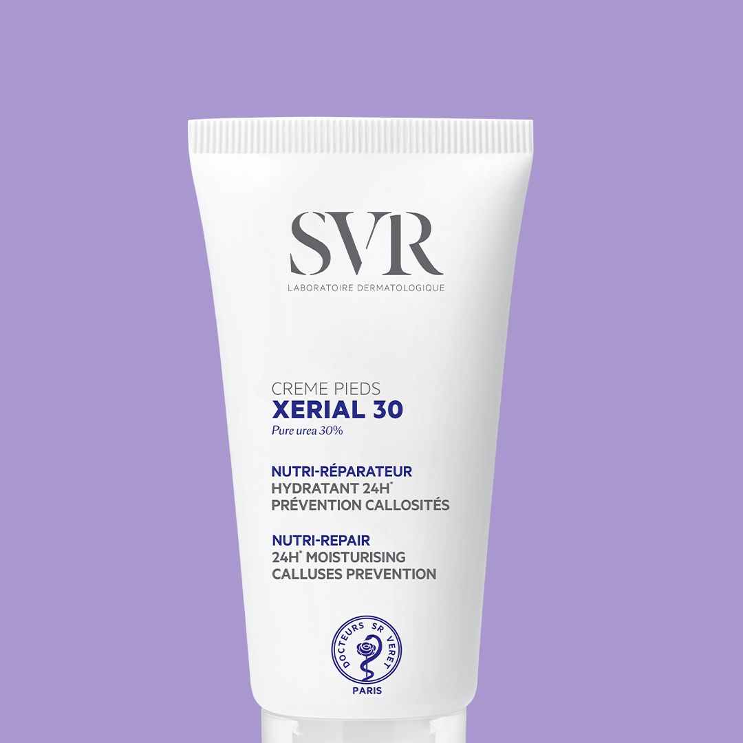 Weiße Tube SVR XERIAL 30 Fußcreme mit blauem Text und Logo vor einem hellvioletten Hintergrund.