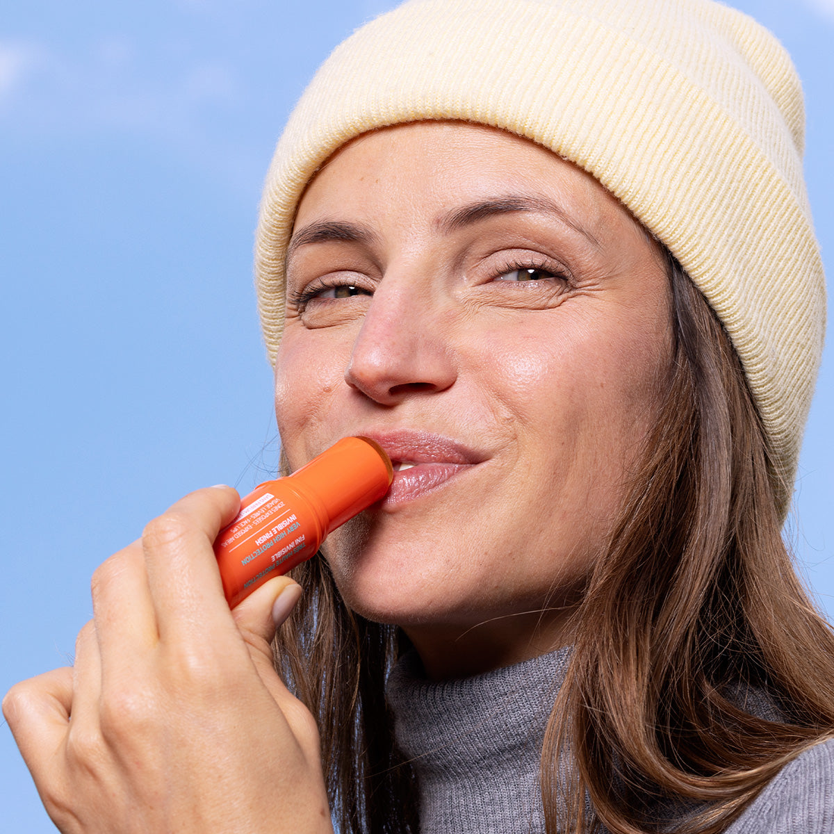 Frau mit gelber Mütze trägt den orangefarbenen Sun Secure Easy Stick SPF50+ auf ihre Lippen auf.